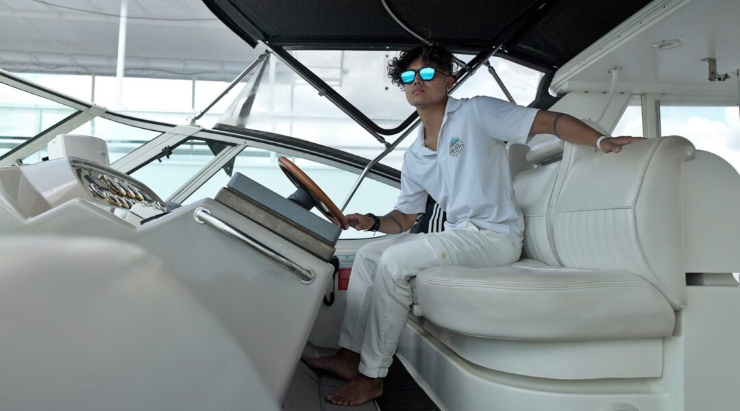 A young male model, sporting stylish GOWOOD wooden sunglasses, relaxes on a luxurious yacht