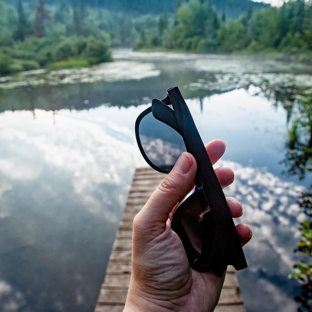 Man holding wooden sunglasses in a lake