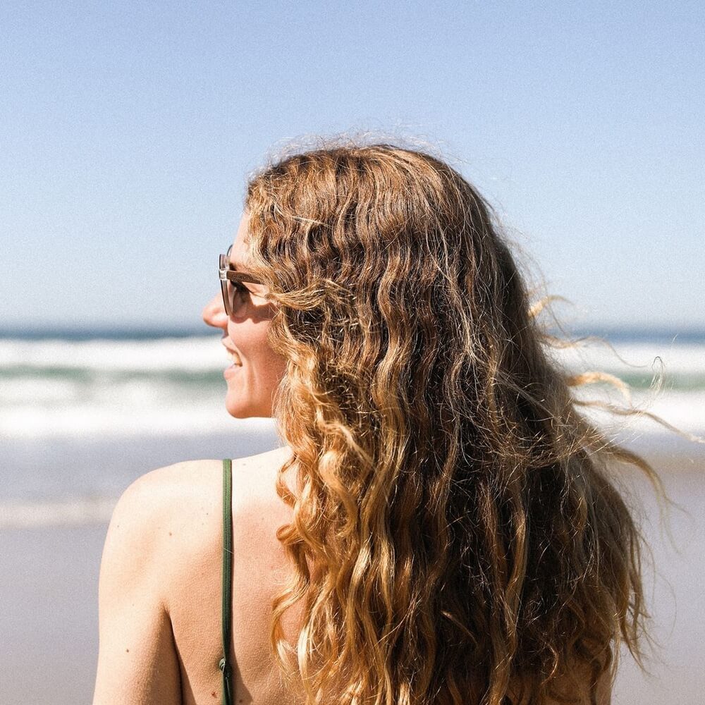 A woman wearing Wayfarer Walnut sunglasses with black lenses at the beach