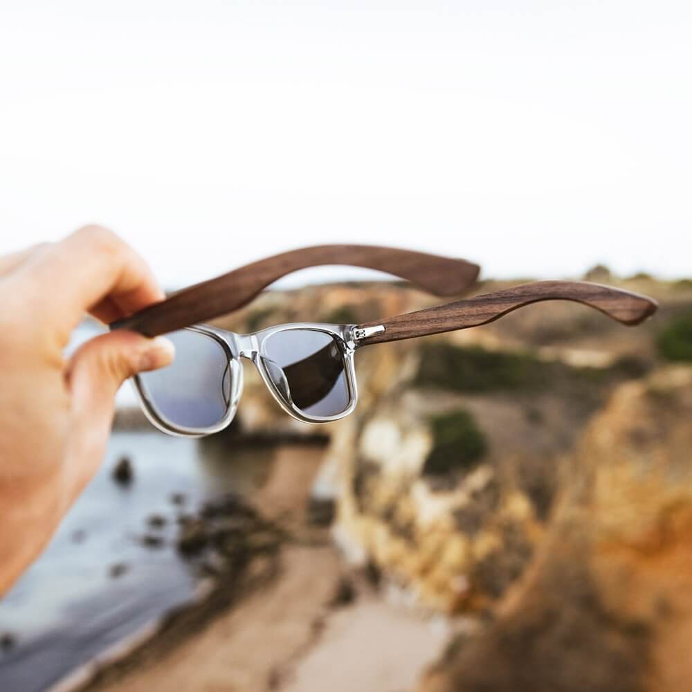 A traveler holding a pair of polarized sunglasses in their right hand, pair from the GOWOOD collection