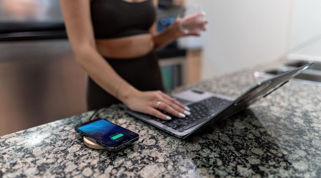 A young woman standing near a wooden wireless charger, working on her laptop