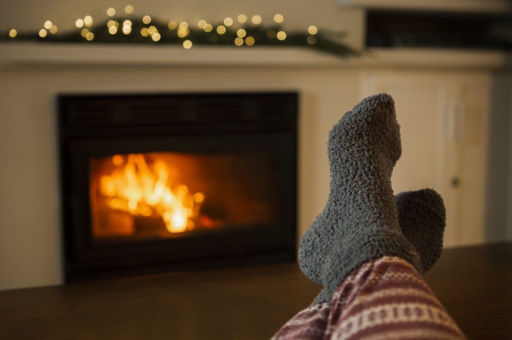 A pair of feet in cozy socks resting in front of a fireplace with a roaring fire