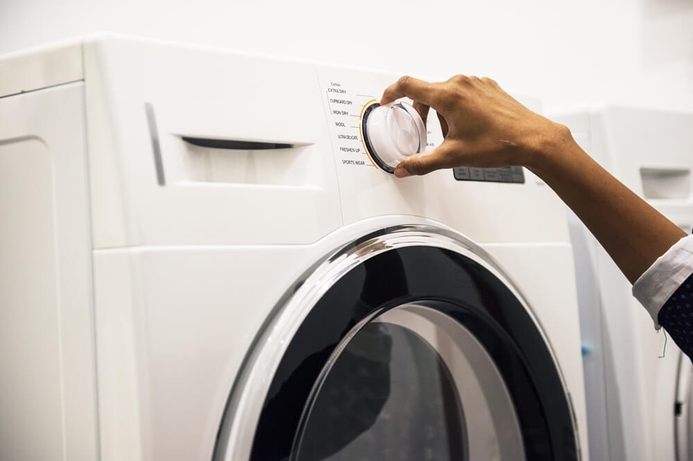 A hand turning the dial on a washing machine to select the desired cycle