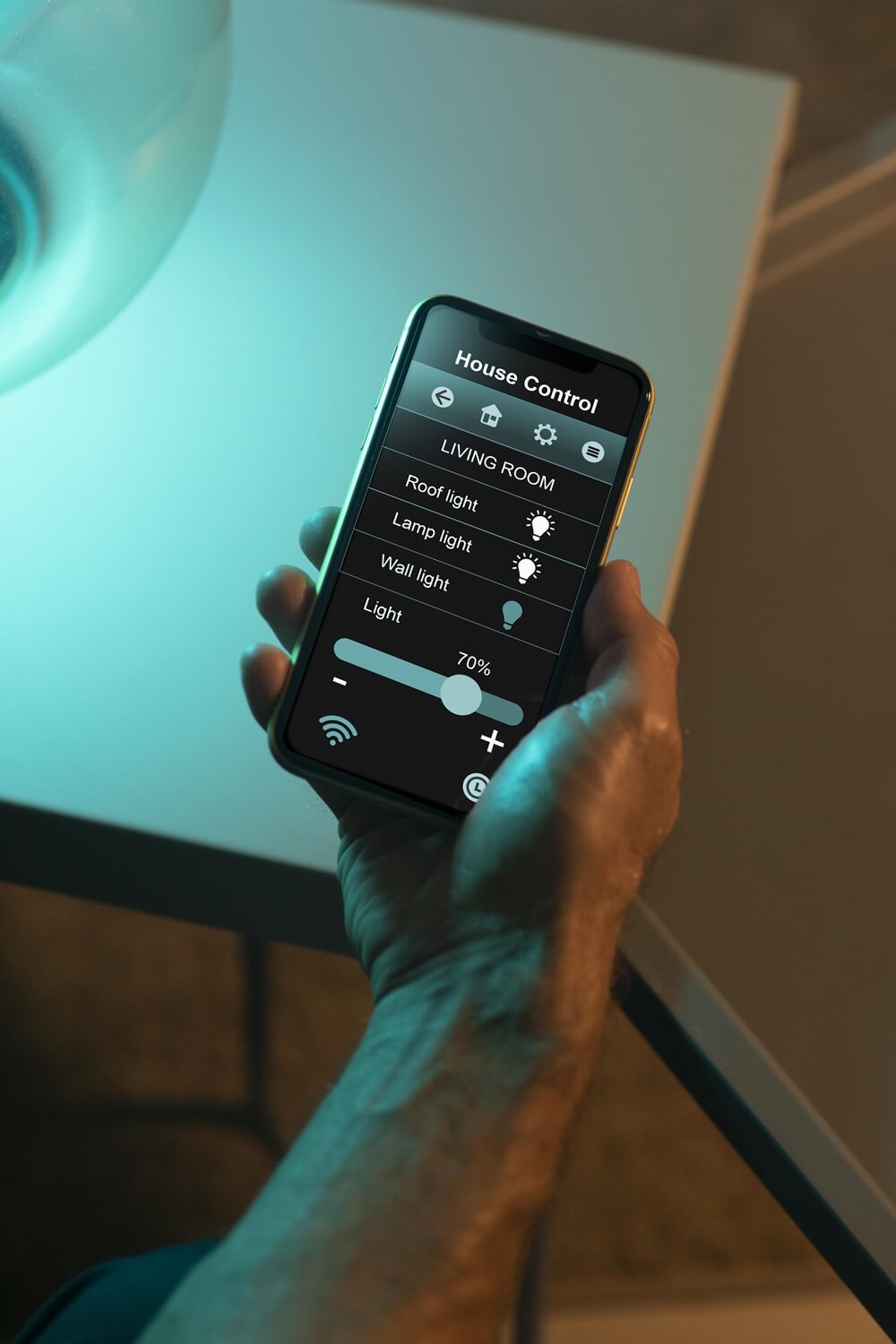 A hand holding a smartphone displaying a home control app with options to adjust living room lights and save energy