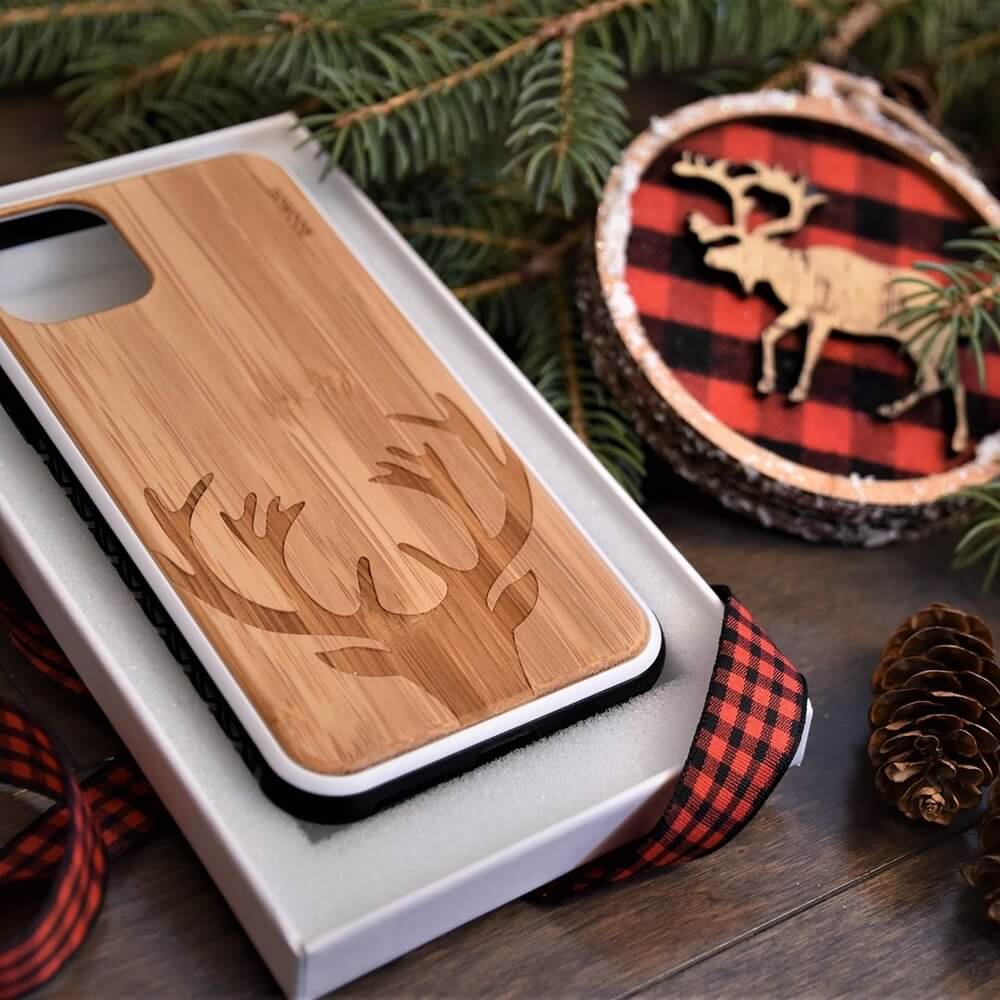 GOWOOD wooden phone case with a reindeer design, resting on a wooden surface with Christmas decorations