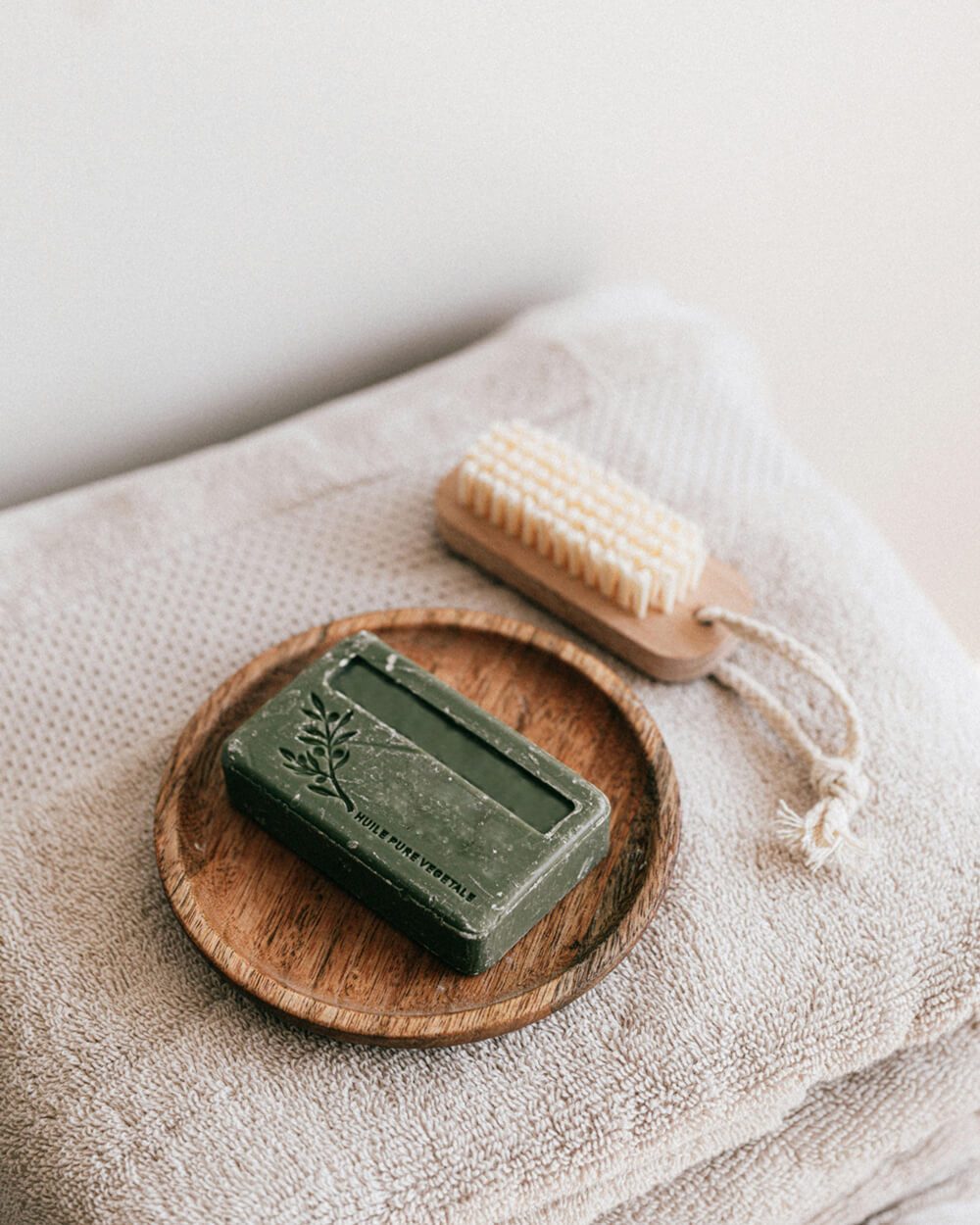 A bar of natural soap on a wooden dish, surrounded by a bath brush and towels