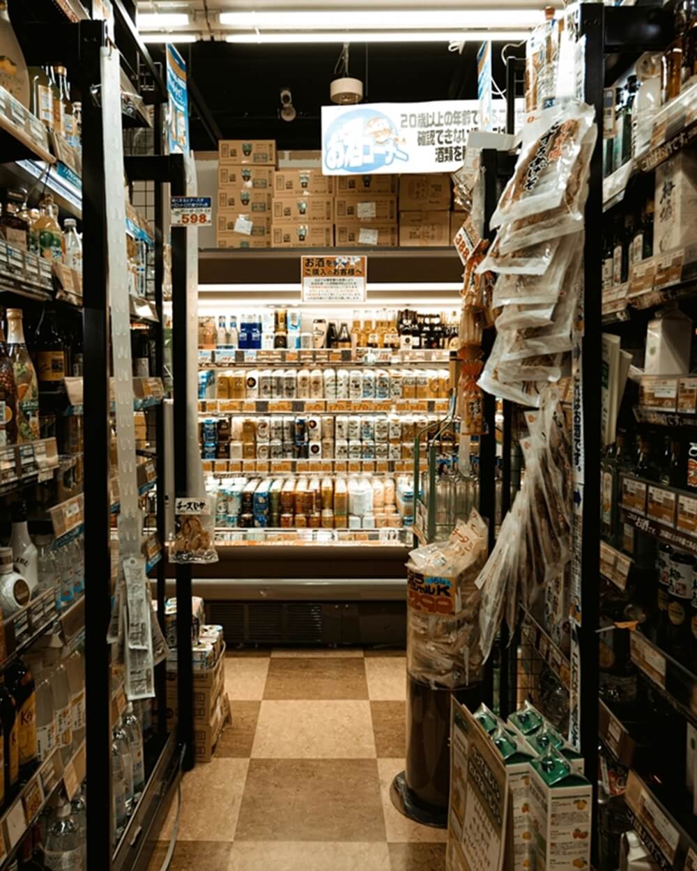 A narrow aisle in a Japanese convenience store, filled with shelves of drinks and snacks