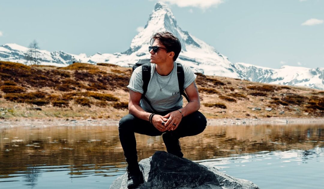 A young man wearing polarized sunglasses in winter while sitting on a bench overlooking a lake